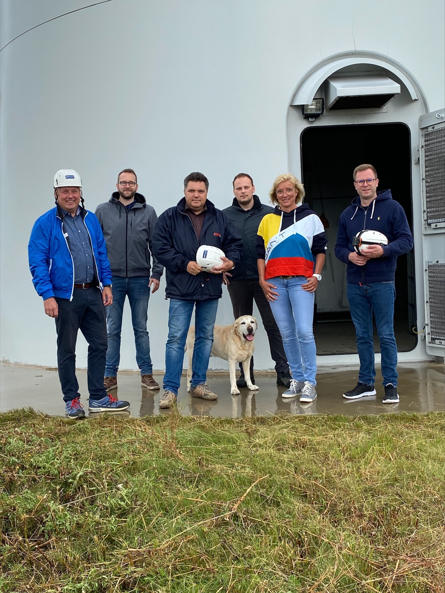An der Windkraftanlage v. l. n. r.: Holger Bormann, Frederik Brandt, Uwe Schäfer, Alexander Kamphenkel, Bärbel Heidebroek und Dr. Adrian Haack